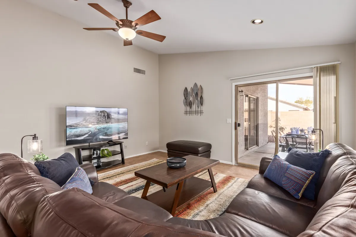 This image features a comfortable living area with a leather sofa, coffee table, TV, and a sliding glass door that offers a view outside. The glass door is a notable feature, serving as a visual connection between the cozy indoors and the outdoor environment, potentially leading to the fenced patio mentioned in the section.