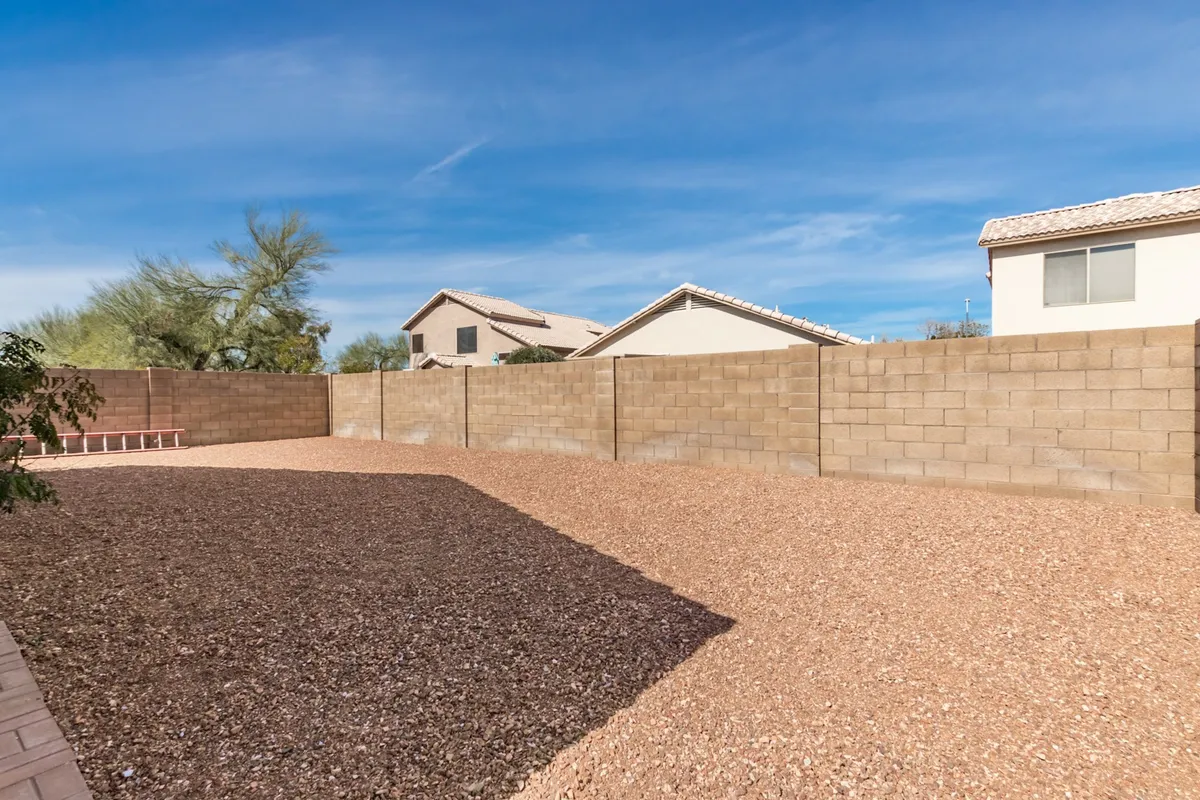 An expansive gravel backyard framed by privacy walls, with residential buildings nearby. The spacious yard offers room for gardening, outdoor gatherings, and children's play, evoking a sense of relaxed community living.