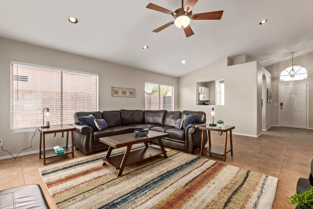 A spacious and inviting living room featuring a large leather sectional sofa, a colorful area rug, a wood coffee table, and decorative wall art. The seating is ample and arranged to foster conversation or cozy movie nights, with an atmosphere of warmth and togetherness.