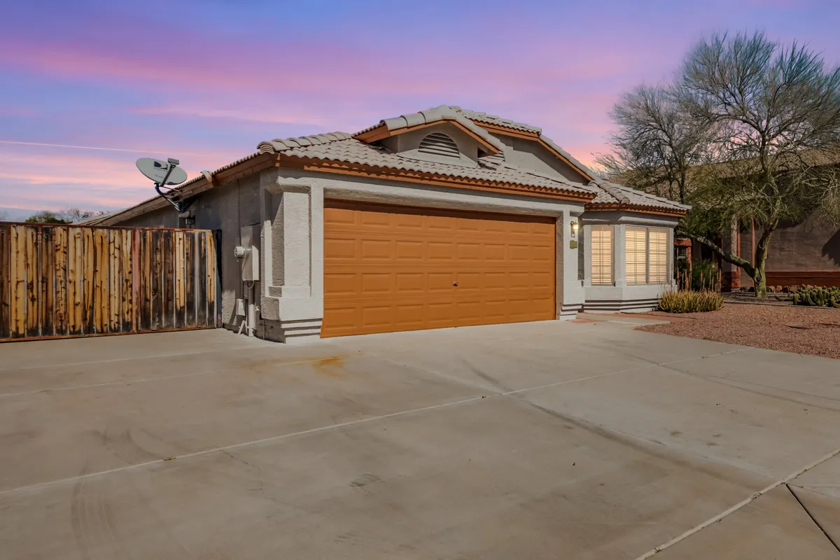 This image showcases the home's inviting exterior, featuring a distinctive orange garage door, large front windows, and a textured wall. The welcoming front porch is perfect for relaxing and watching sunsets, hinting at the lifestyle awaiting just outside the door.