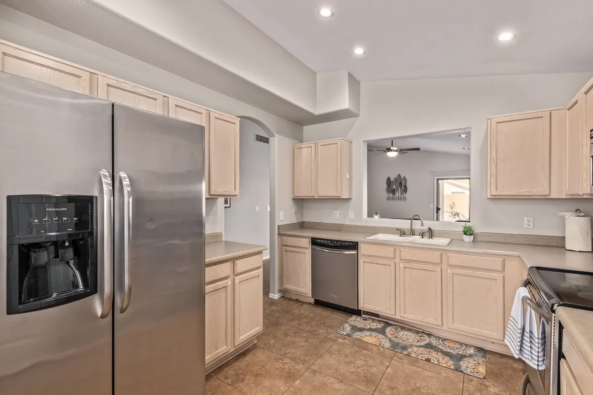 A bright, inviting kitchen featuring stainless steel refrigerator and sink with a window view, wood cabinetry, and spacious countertops. The scene evokes the joy of cooking, gathering, and entertaining, with natural light enhancing the welcoming atmosphere.