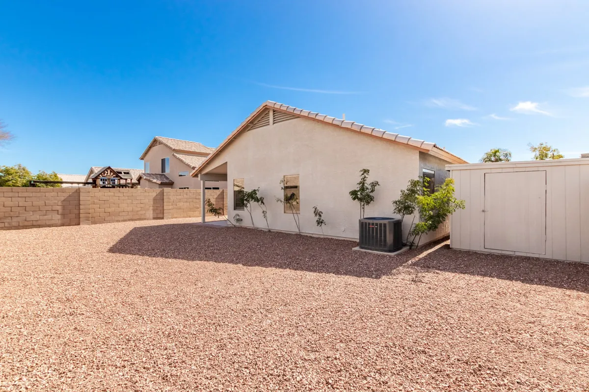 This image showcases the exterior of the vacation home, featuring a welcoming gravel yard, lush plants, and the house itself bathed in warm sunset light. The peaceful, open setting hints at spacious parking and an inviting atmosphere for gatherings before or after outings.